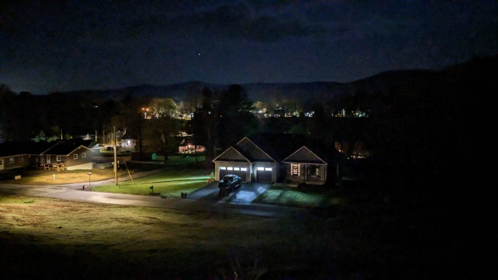 A night sky with a faint view of small houses with their lights on dotting the horizon.