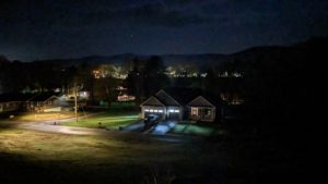 A night sky with a faint view of small houses with their lights on dotting the horizon.