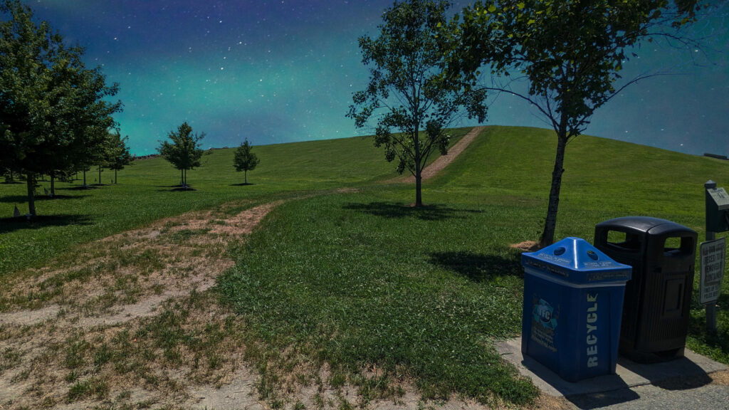A landscape picture with a dirt path leading up a hill. The horizon is a sky similar to that of the northern lights.